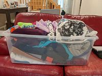 Plastic bin filled with assorted fabrics in various colors and patterns placed on red leather couch