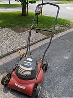 Front and side view of red and black Homelite electric lawn mower showing handle, wheels, and brand name.