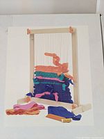 Photo of the weaving loom in use showing colorful fabric being woven on the wooden loom frame with yarns and weaving tools in front