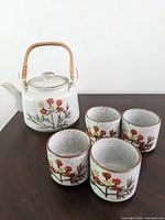 Teapot with four cups arranged together showing floral design and woven handle.