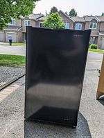 Front view of the black Insignia mini fridge closed, showing minimal wear and the brand name on top right.