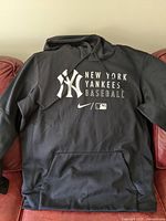 Front view of black New York Yankees men's XL hoodie sweater laid flat on couch showing all logos and text on front