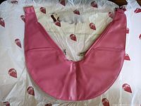 Pink synthetic crescent-shaped sash bag laid flat on white tissue paper with red logo prints, showing front zipper compartments.