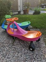 Photo showing the pink and orange plasma bike in front of the blue and green plasma bike outdoors on gravel, highlighting the full shape and colors.