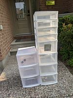 Front view of two plastic storage drawer units, one with 3 drawers and one with 6 drawers, placed on a concrete surface near a front door.