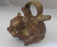 Side angle close-up showing the rodent figure's face, limbs, and one spout, highlighting the textured ceramic surface and coloration.