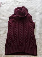 Sleeveless red cable knit turtleneck sweater spread on light background showing knit pattern and shape