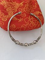 Front view of open silver cuff bracelet with three silver spheres and patterned accents on an orange-gold embroidered pouch