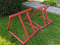 Two red plastic skate aids on grass, shown from front side.