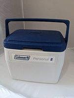 Front view of Coleman Personal 8 cooler showing blue lid and handle with white body and branding.