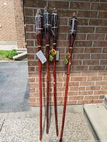 Four new Tiki torches leaning against a brick wall, showing their full length and design including tags and wrapping on some torches.