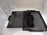Two black perforated metal roasting pans set side by side showing size difference and handles