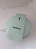 Closed light green Thinkkitchen pancake maker with brand name on top, showing handle and power cord.