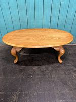 Full view of the oval solid oak coffee table showing natural wood grain and three curved Queen Anne style legs.
