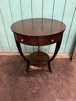 Full view of Maitland Smith ebony veneer round side table with tripod curved legs and drawer.