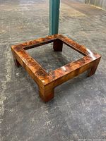 Front angle view of the large square coffee table base in tortoise shell burl walnut finish on concrete floor with no glass top.
