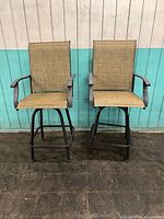 Pair of two metal-framed outdoor slingback barstools, front view against a white and teal paneled background.