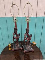 Pair of vintage table lamps with monkeys climbing bases, displayed on a table against a blue and white wooden wall.