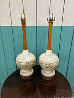 Front view of the pair of vintage Mid-Century Modern incised ceramic and wood table lamps on a wooden surface.