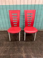 Front view of two red vintage side chairs with metal frames arranged side by side against a blue wooden wall.