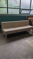 Full view of tan 3-seater sofa with wooden legs against a windowed wall.