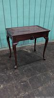 Front angle view of vintage mahogany Queen Anne style tea table showing carved apron, cabriole legs and pull-out tray on right side.