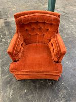 Front view of a vintage lounge armchair upholstered in orange velvet with button tufting and plush arms and seat cushion.