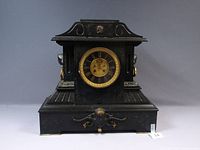 Front view of black slate case mantel clock with gilt decorations and brass dial