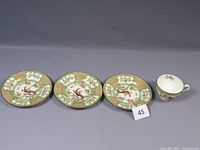 Three porcelain plates and one teacup shown together displaying the full set and design consistency.