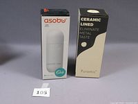Two Asobu Puramic Orb bottles in original packaging, one black and one white, both ceramic lined.
