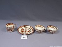Four pieces of Copeland Spode Indian Tree Rust Orange pattern including three cups and one plate arranged to show front patterns.