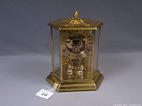 Full angled front view of Elgin anniversary clock showing gold-tone metal hexagonal case with glass panels and decorative finial on top.