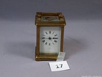 Full frontal view of the brass French carriage clock showing the white face with Roman numerals and black hour and minute hands.