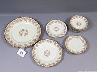 Set of 9 white porcelain plates and bowls with pink bridal rose floral pattern and gold scalloped edges.
