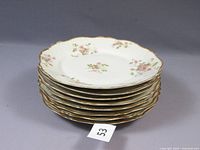 Stacked view of eight white Limoges dinner plates with pink floral patterns and gold scalloped rims.