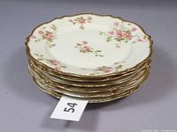 Stack of six scalloped edge salad plates with pink flowers and gold rims, stacked to show the shape and floral pattern.
