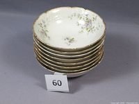 Stack of eight Limoges porcelain bowls showing scalloped edges with purple floral patterns and gold trim.