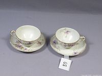 Two porcelain cups with matching saucers, purple flower decoration and gold trim, placed side by side with lot number 59 in image.