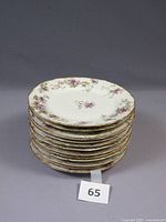 Stack of twelve Limoges salad plates decorated with purple flowers and gold trimming.