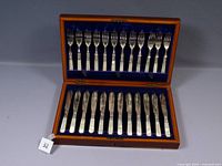 Full view of the flatware set in open polished wooden box with blue velvet interior, showing 12 knives and 12 forks.