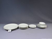 Image of Rosenthal Crown Jewel dinnerware set showing dinner plates, luncheon plates, bread plates, and saucers stacked and arranged on gray background.
