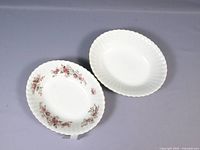Two oval serving bowls side by side on a grey cloth background, showing both plain white bowl and floral bowl with rose pattern.