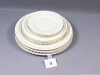 Stacked plates showing different sizes from bread to dinner plates with gold rim and scalloped edges.