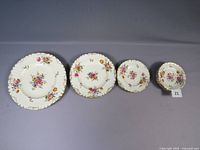 Four Royal Crown Derby Posies dish plates arranged in a row by size: dinner plate, luncheon plate, bread plate, saucer. White porcelain with colorful floral posies and gold trim. Photo taken to show detailed design and size progression of plates.