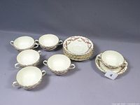 Set of six cream soup bowls and six matching saucers arranged on surface, showing full lot contents