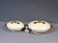 Two white serving bowls tureens with lids, gold handles and decorative accents on a flat surface