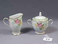 Front view of the creamer and sugar bowl set showing floral design, gold trim, and overall condition