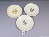 Three vintage dinner plates with floral designs: two with red berries on black stems, one with yellow wheat and white flowers.