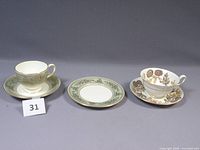 Three items shown in the lot: Columbia cup and saucer with sage green and gold trim, plate with matching pattern, plus Lichfield cup and saucer with floral botanical design.