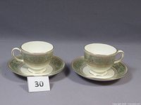Two Wedgwood Columbia cups and saucers in sage green with gold detailing set side by side on a neutral background.
